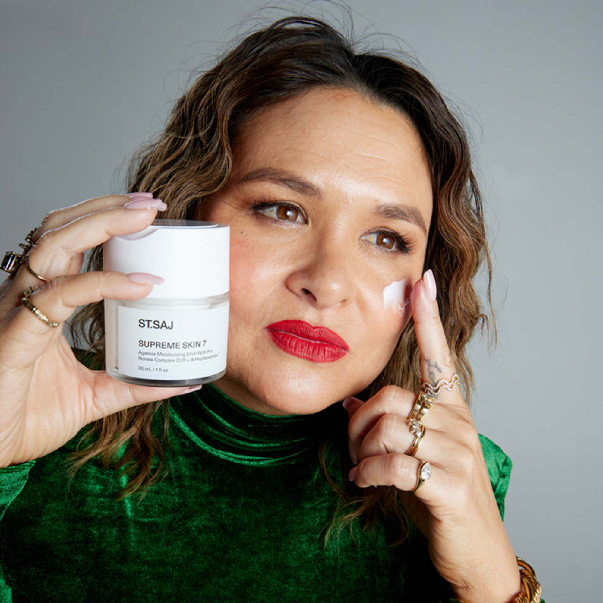 Founder Emmylou in green cloth holding ST.SAJ Supreme Skin 7, touching face.