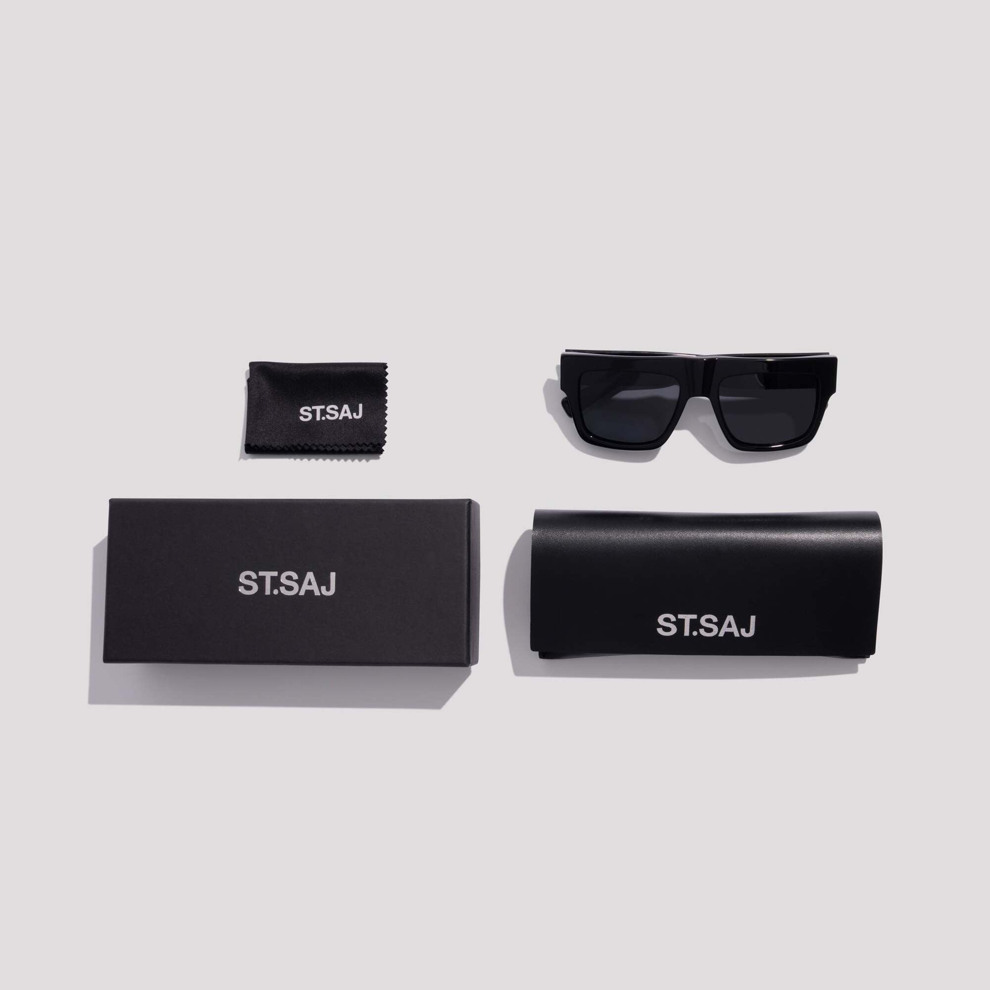 ST.SAJ Eyewear SS01 with black hard case and lens cloth flat lay on grey background.