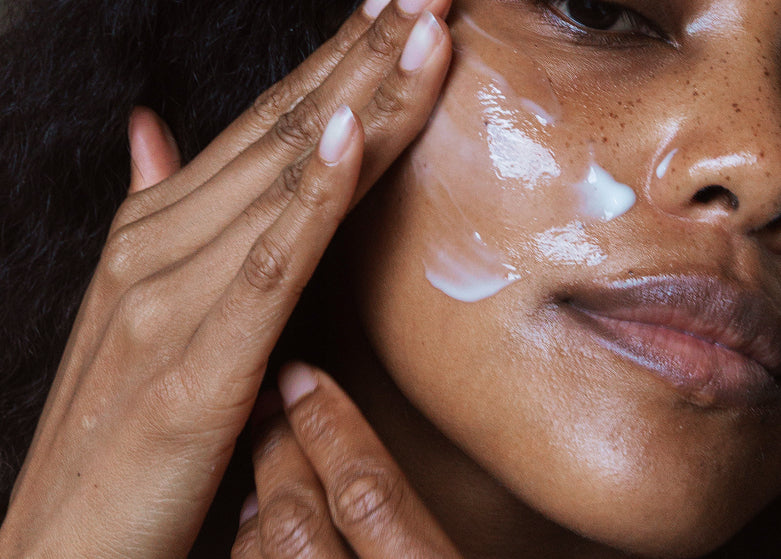 Close-up of a person applying cream to their face with a hand.