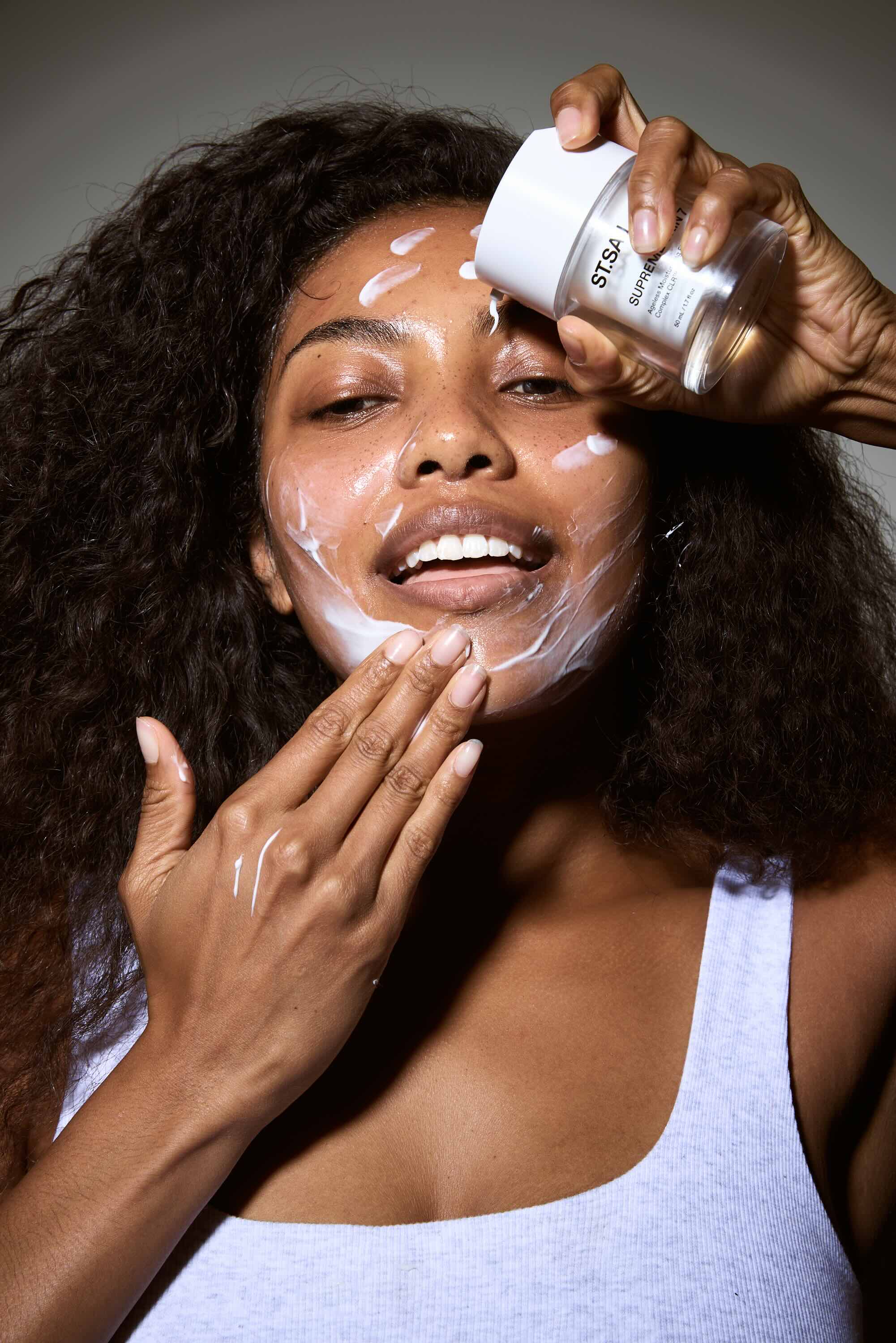 Woman applying facial cream to her face with a neutral background