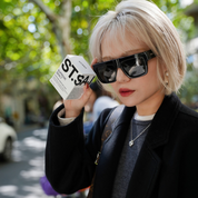 Female model wearing ST.SAJ SS01 Oversized Sunglasses, holding Supreme Skin 7 box outdoors.