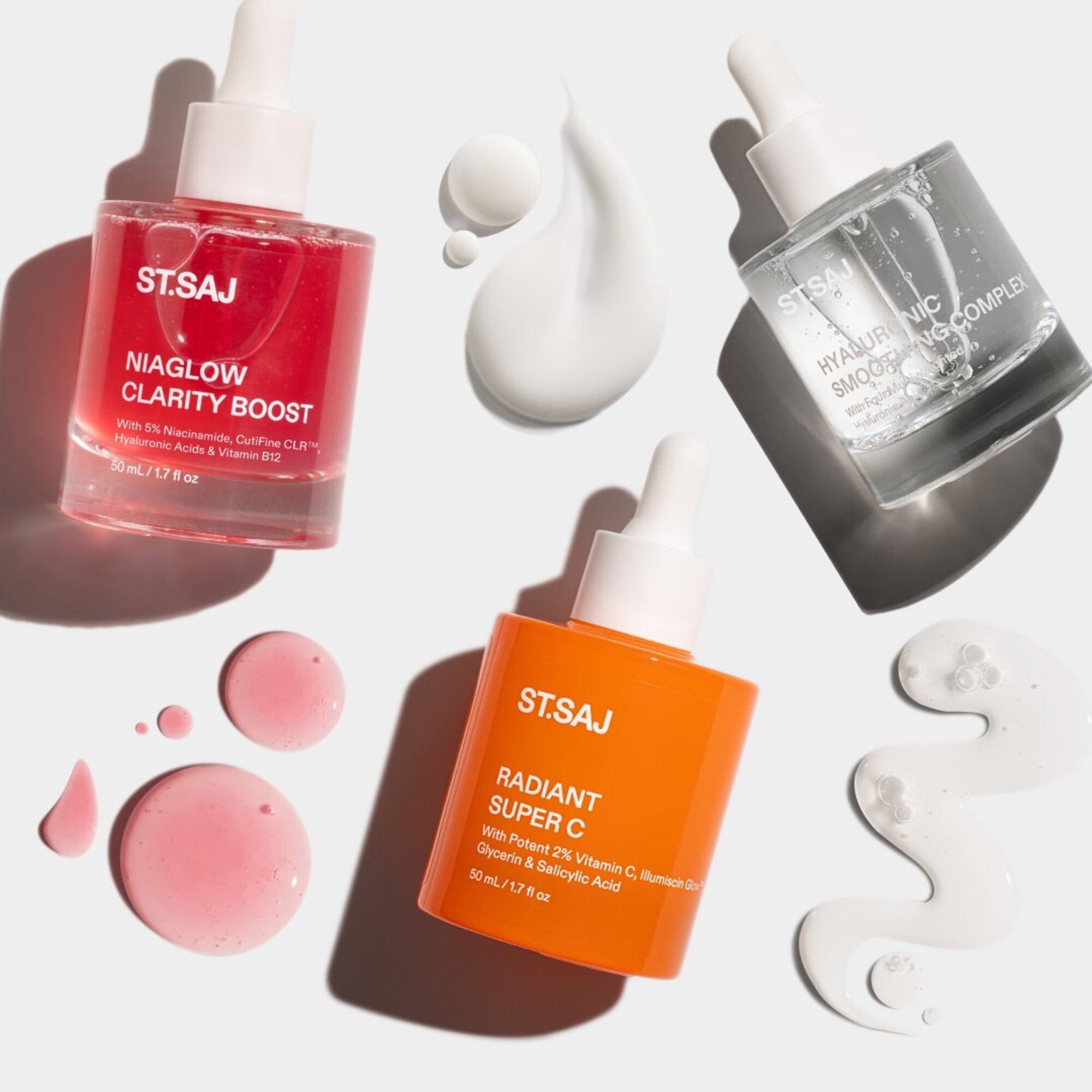 ST.SAJ Niaglow Clarity Boost, Radiant Super C and Hyaluronic Smoothing Complex bottles with serum swatches on grey background.