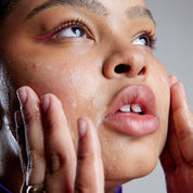 Close-up of woman with glowing wet skin touching her face.