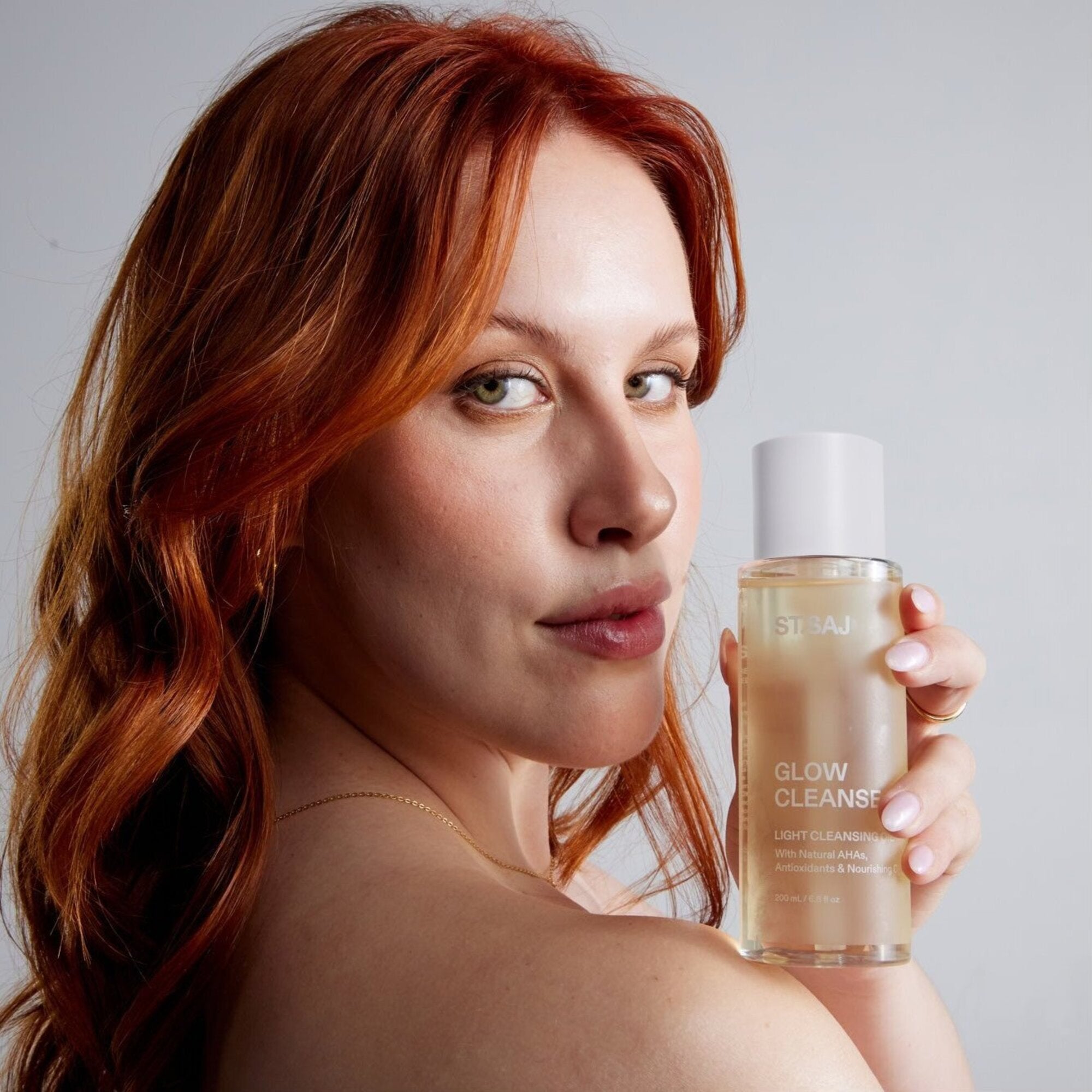 Red-haired woman holding ST.SAJ Glow Cleanse.